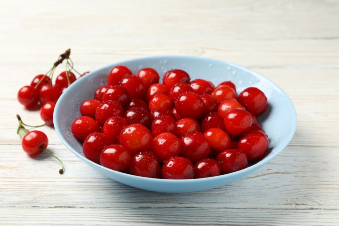 Plate with red cherry on wooden background, close up