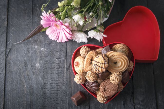 Heart shaped gift box with sweets and flower bouquet on wooden table