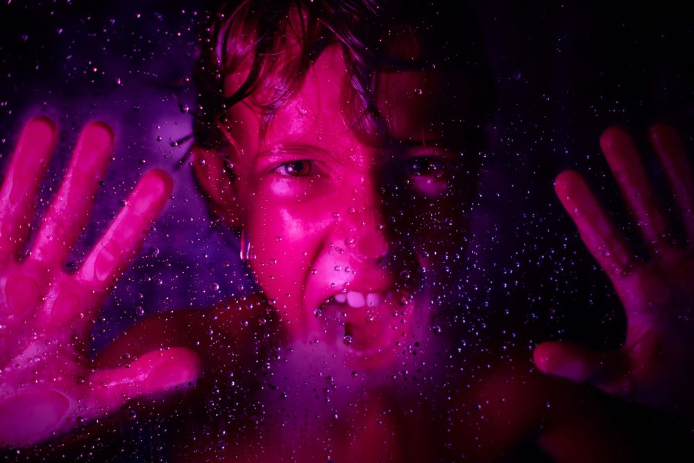 Crop angry boy screaming behind wet glass wall