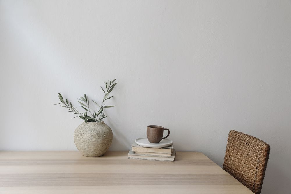 Wooden table with wicker chair, books, mug and vase