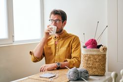 Man drinking hot tea during knitting