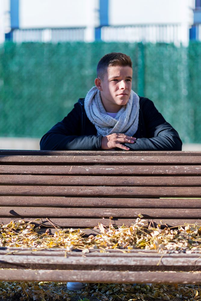 Teenage male sitting behind a wooden bench in a city park