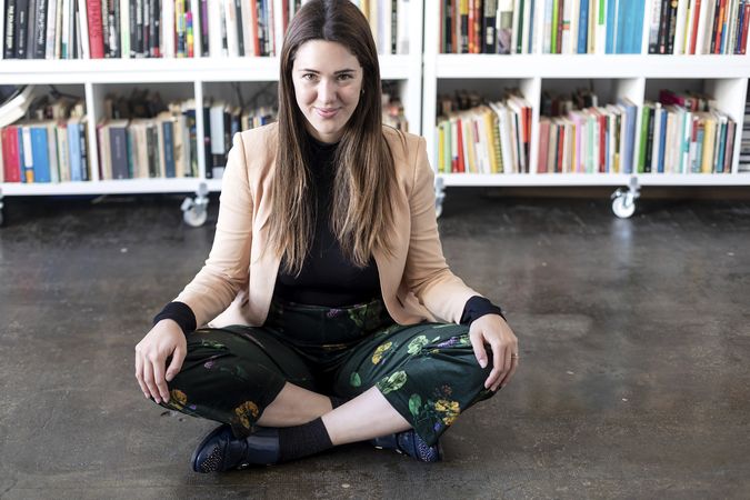 Portrait of a smiling woman sitting cross legged in front of book shelf with copy space