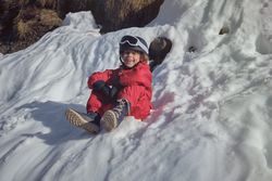 Cheerful kid sitting on snow in mountains