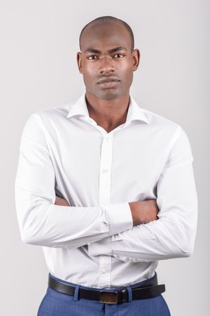 Serious male in button up shirt with arms crossed against a plain wall