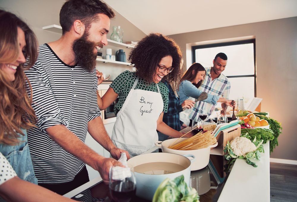 Group of friends cooking in a bright kitchen with recipe books