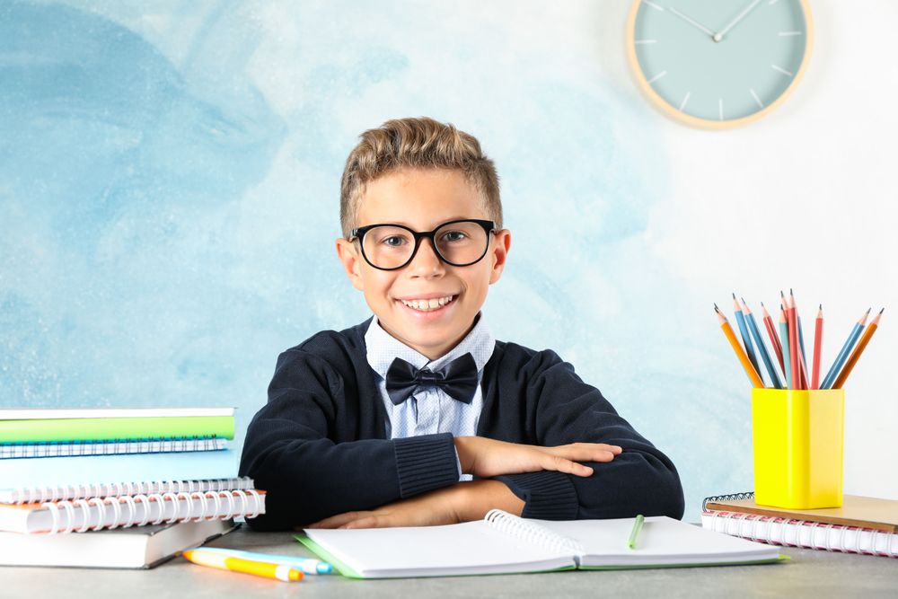 Boy in school uniform sitting at the table against color background