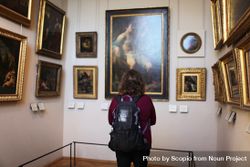 Back view of a person with backpack looking at a painting in a museum 4NJgr4