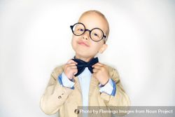 Blond boy making an inquisitive face wearing round glasses and fixing his bow tie 4Mpxy5