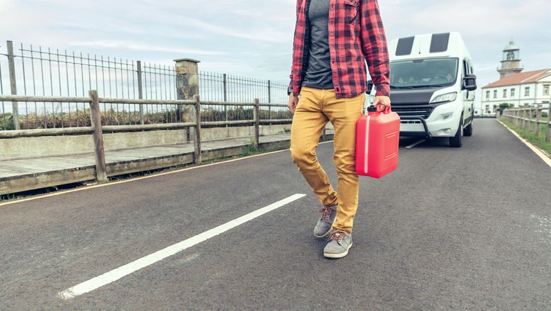 Male in red checkered shirt walking in front of parked van with gas can
