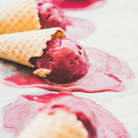 Close up of cones of dark berry ice cream melting on marble slab, square crop