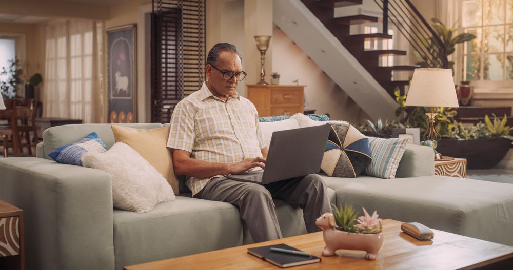Mature Indian Man Using Laptop at Home: Using Online Platforms to Explore His Interests, Delving into History, Arts, and Literature.