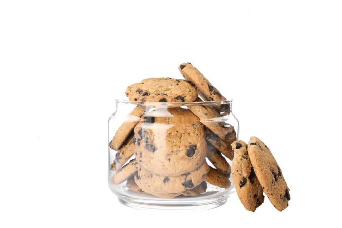 Glass jar with tasty chocolate chip cookies on studio background