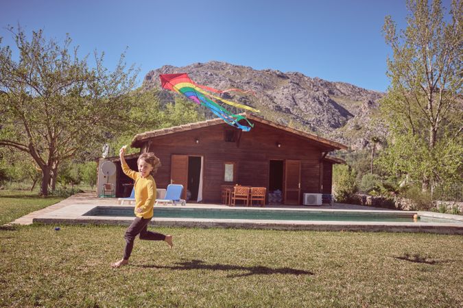 Boy playing with colorful kite near wooden barn
