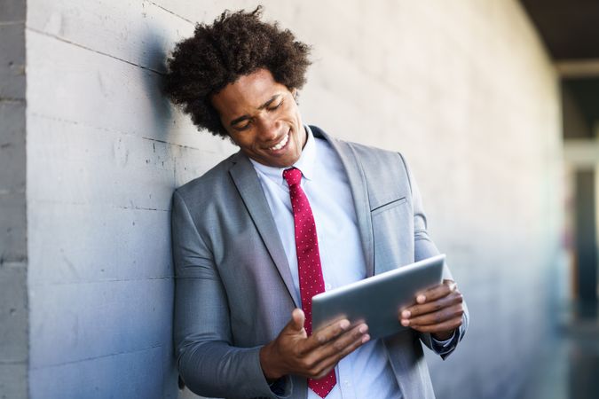 Man smiling at his tablet leaning on wall