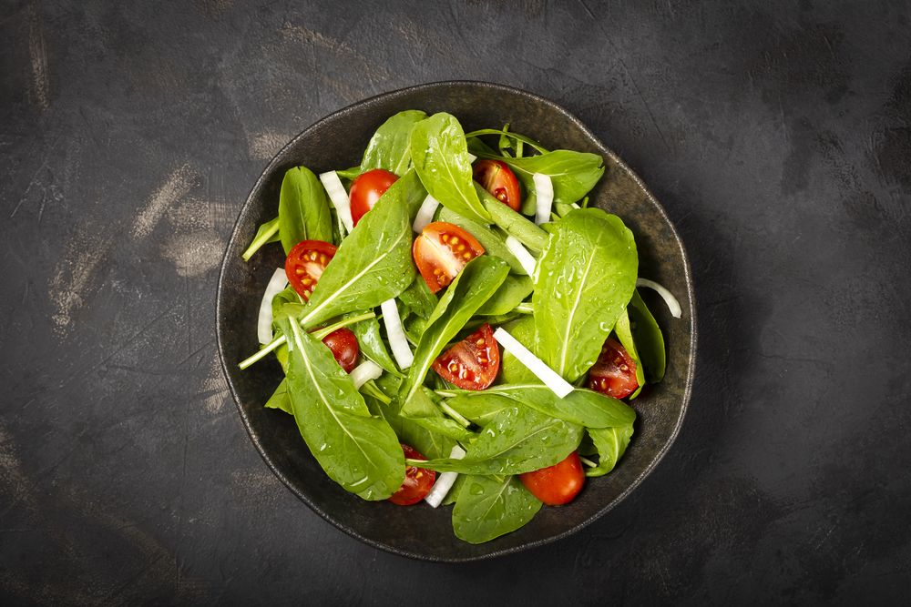 Arugula salad with tomatoes on dark background.