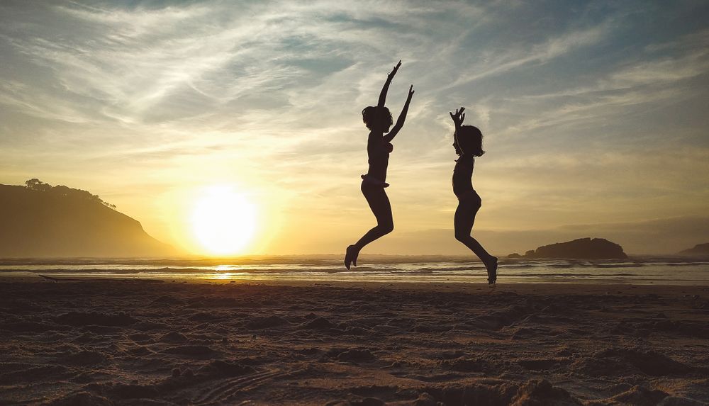 Silhouettes of two little girls jumping in the beach at sunset