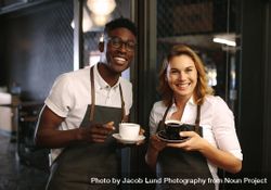Male and female barista standing at the entrance of coffee shop holding coffee cups 4Ax9E5