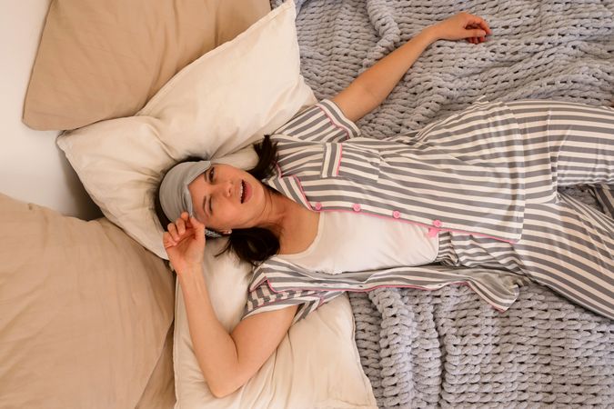Woman laughing while lying in bed, wearing eye mask.