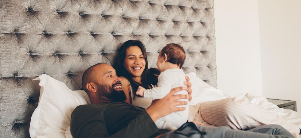 Happy parents playing with their newborn son on bed at home
