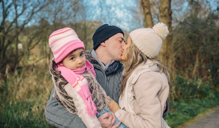 Father holding daughter a he kisses wife