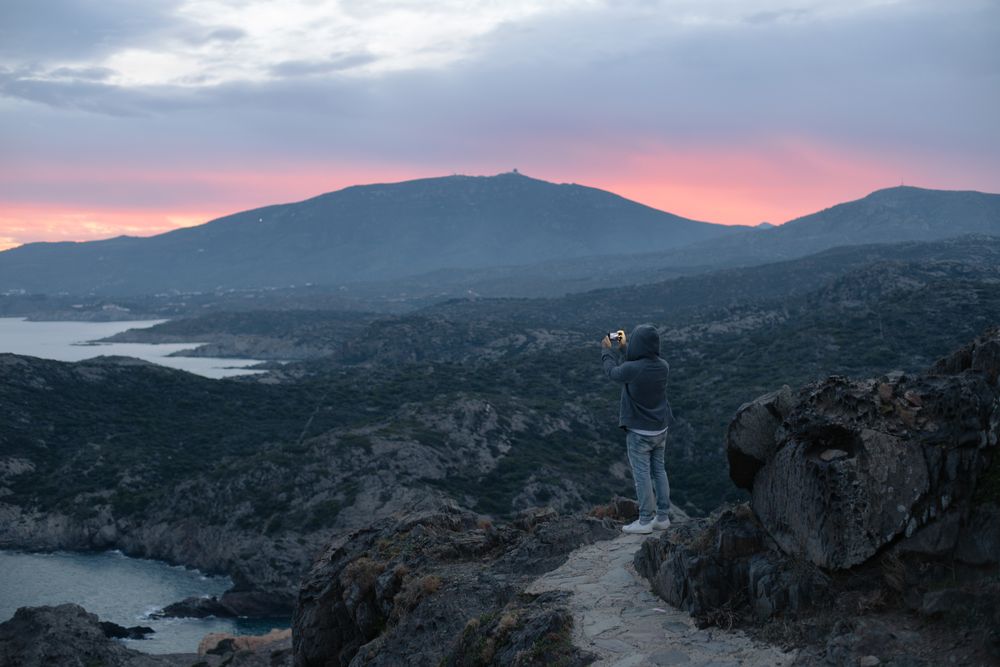 Male taking photo on cliff at sunset