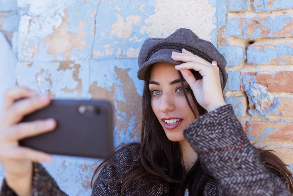 Charming Hispanic lady taking selfie near wall