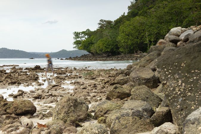A young woman walks barefoot among the rocks of Gapang beach, on the island of Pulau Weh, Indonesia