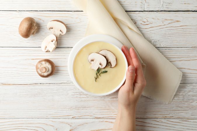 Hand holding a bowl of of creamy soup on table