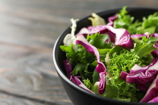 bowl with fresh vegetable slices on wooden background, close up