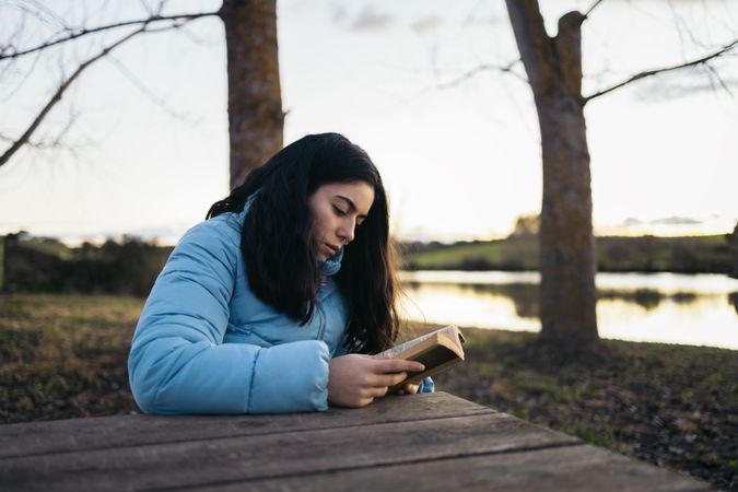 Woman reading a book outdoors near a lake