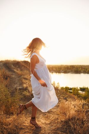Blonde female in ethereal summer dress looking back at lake