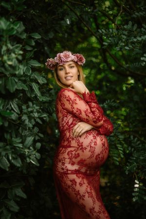 Pregnant woman with closed eyes touching belly and chin while standing in garden in sunny day