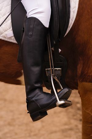 Equestrian leg in stirrup, riding attire, close-up.