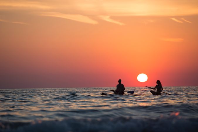 Silhouette of man and woman paddling on sea during sunset
