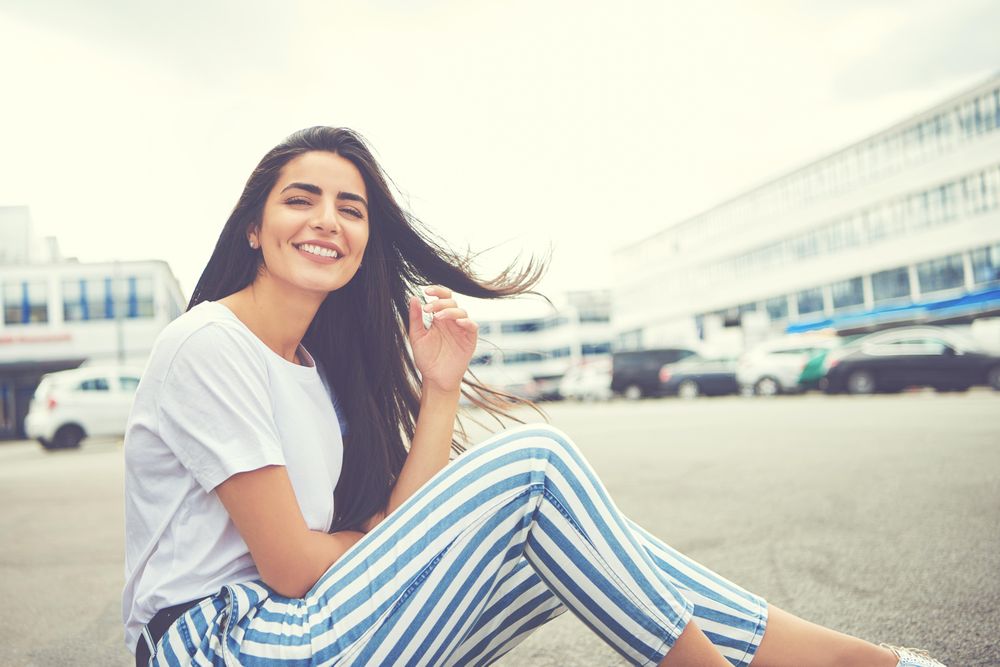Happy woman sitting on curb with brown hair blowing in the wind