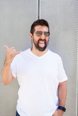 Latino man in sunglasses making rock on sign outside