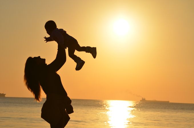 Sideview of mother holding a baby near seashore at sunset