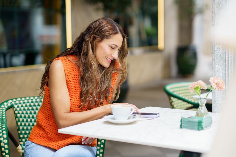 Woman using phone sitting on the terrace of a cafeteria