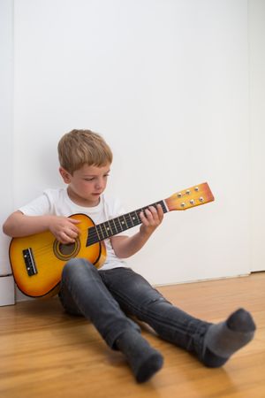Young blonde boy playing toy guitar