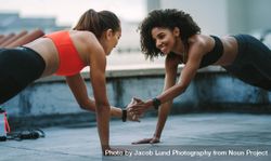 Smiling fitness women doing push ups on rooftop facing each other 493PE0