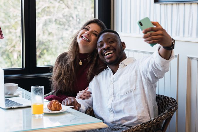 Cheerful multiethnic couple using laptop at home while taking a selfie
