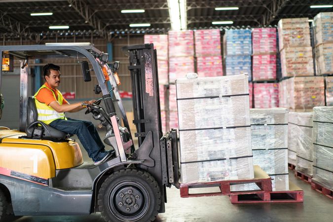Man driving forklift iand moving merchandise in distribution center
