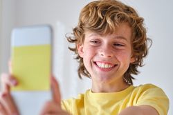 Cheerful boy taking selfie on smartphone on light background