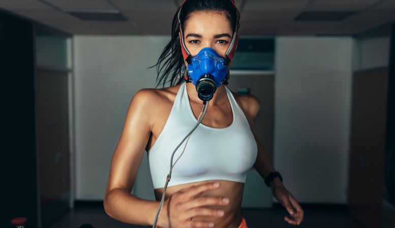 Portrait of athletic woman with mask running on treadmill in gym