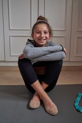 Cheerful girl wearing gymnastics slippers sitting on yoga mat