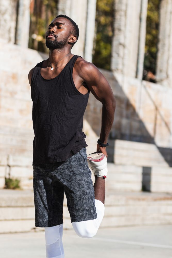 Black sportsman stretching on basketball court