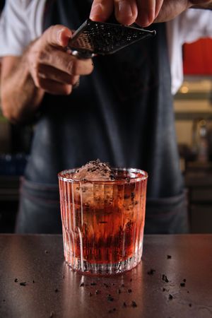 Unrecognizable bartender grating chocolate on Negroni cocktail
