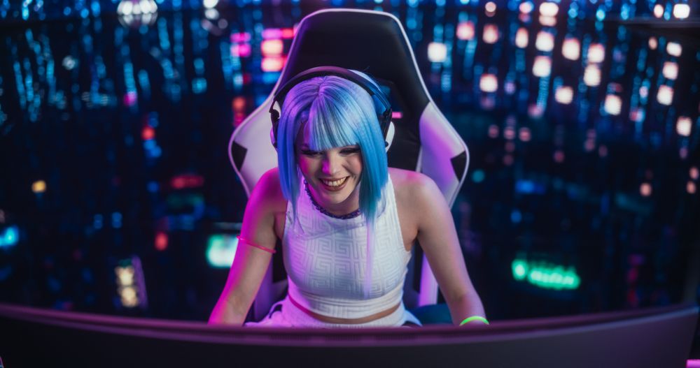 Smiling Cosplayer Talking to Her Online Friends on Desktop Computer While Sitting in Futuristic Cyberpunk Home.