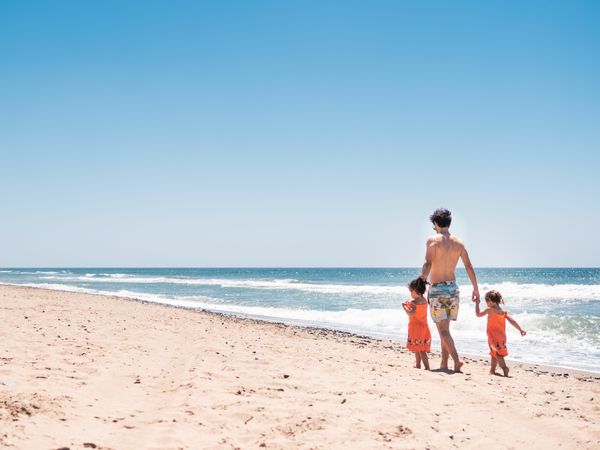 Father walking on sandy beach with toddler daughters